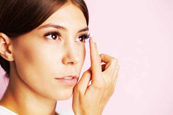 A woman putting on contact lenses on pink background